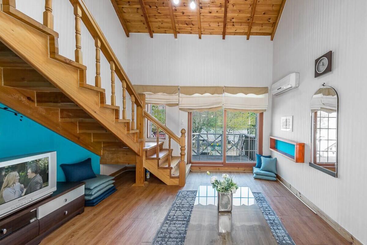 A spacious living room with a wooden staircase, a television, a sofa, and a large window.
