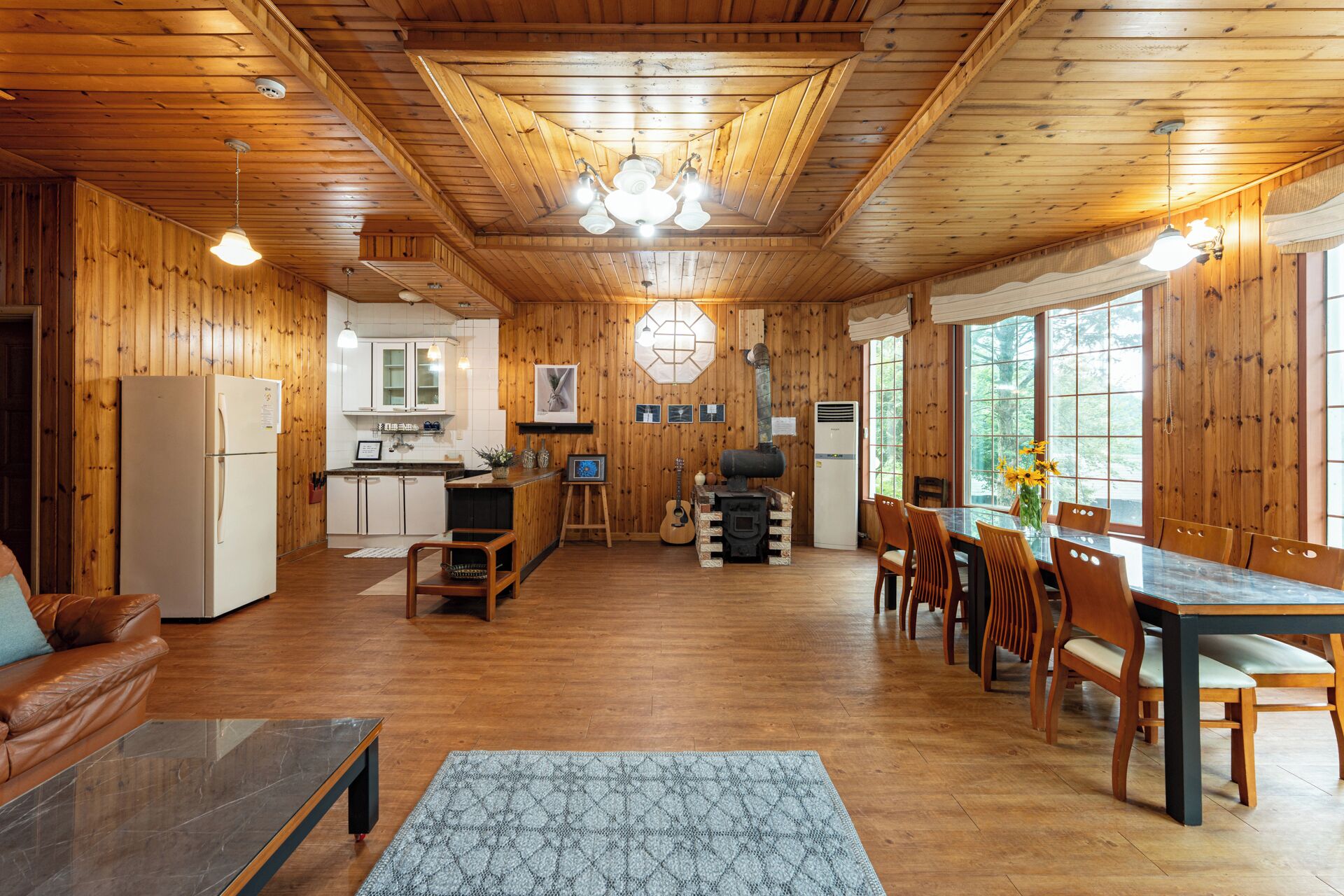 A cozy cabin interior with wooden walls, a kitchen area, a dining table with chairs, and a fireplace.