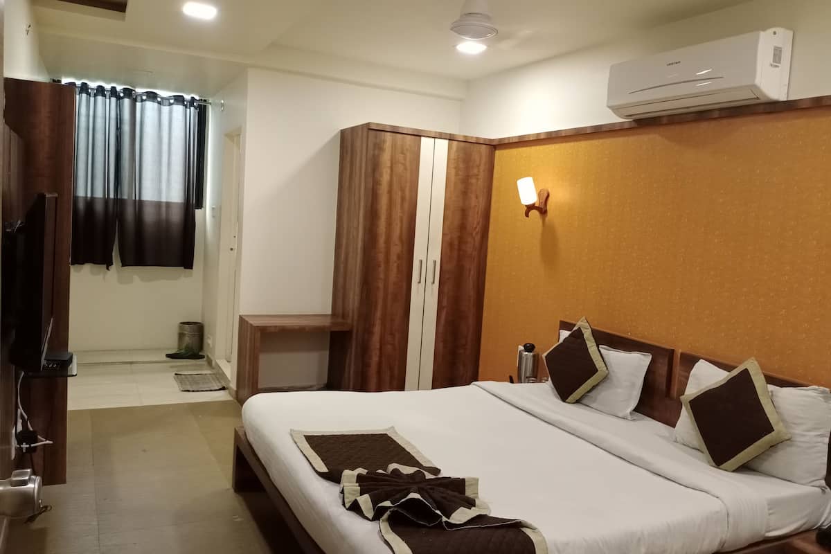 A hotel room with a bed, a wardrobe, a desk, and an air conditioning unit.