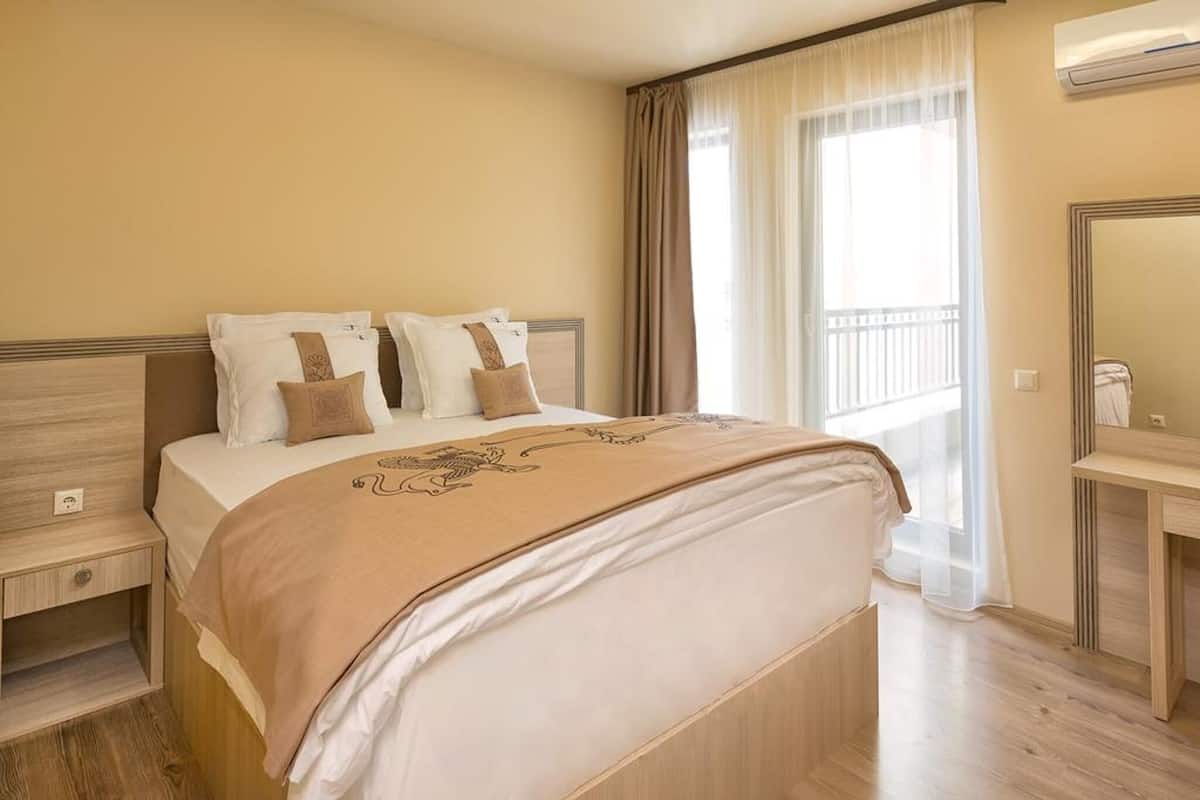 A hotel room with a bed, a bedside table, a mirror, and a window with curtains.
