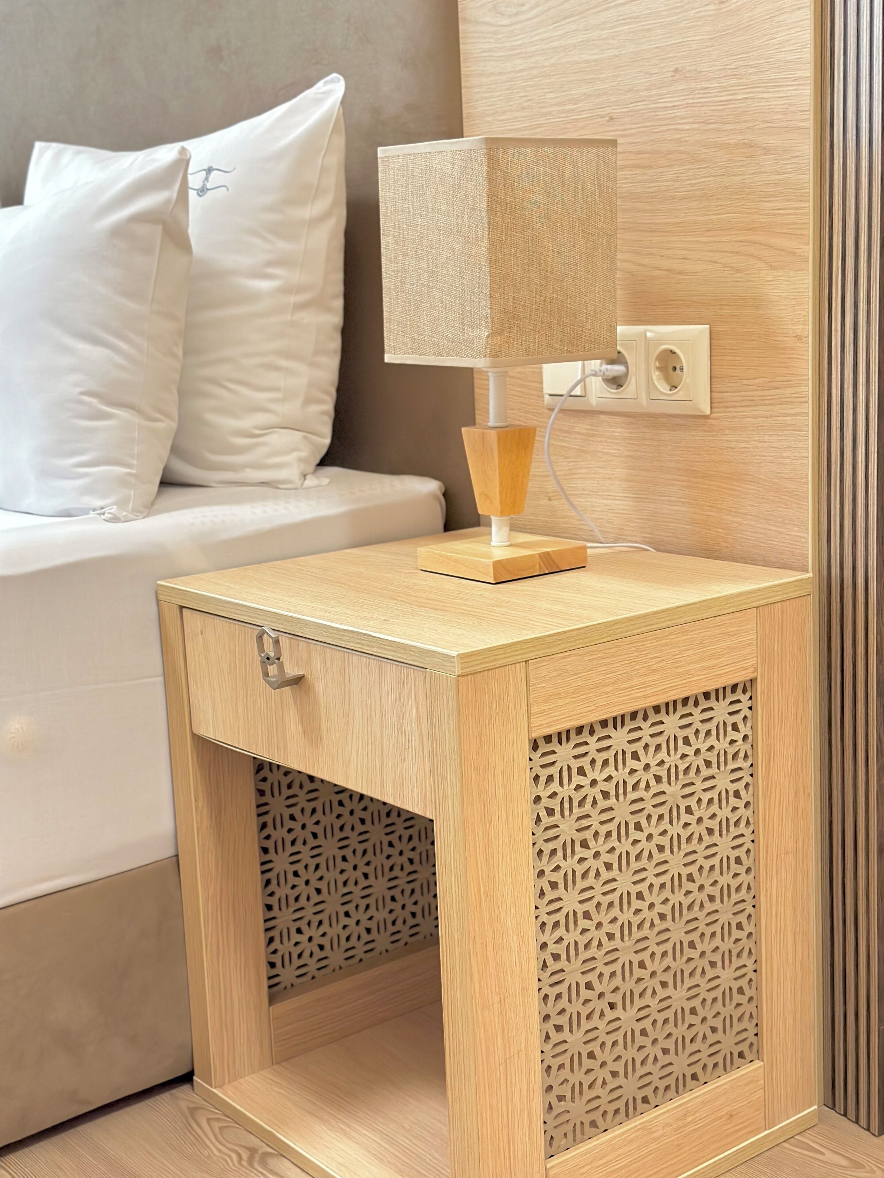 Une table de chevet en bois, dotée d’une lampe, d’une prise électrique et d’un panneau décoratif.