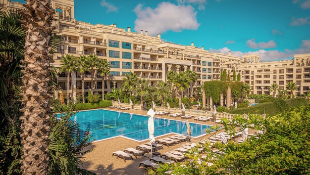 A hotel with a swimming pool, palm trees, and a multi-story building.