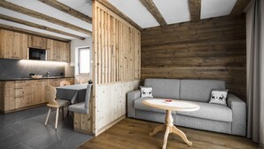 A modern kitchen with wooden beams, a grey sofa, and a round wooden table. - MAGNIFICENT CHALET COMFORT AND MODERNITY: OUR APARTMENTS IN PUSTERTAL (St. Lorenzen)