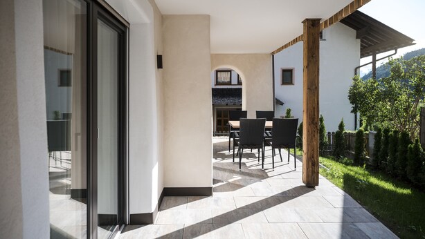 A modern patio with a dining area, a glass door entrance, and a view of a mountain. - MAGNIFICENT CHALET COMFORT AND MODERNITY: OUR APARTMENTS IN PUSTERTAL (St. Lorenzen)