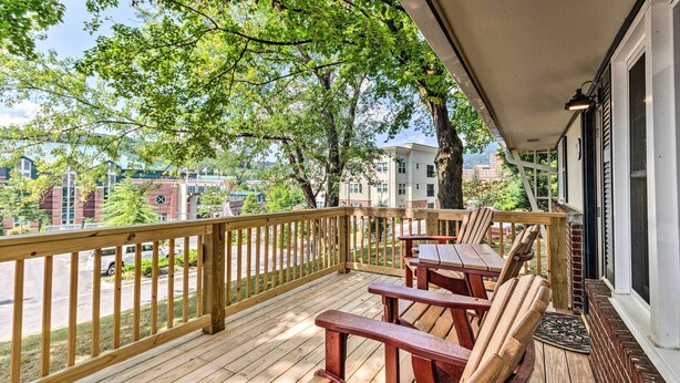 Una terraza de madera con vistas a un paisaje urbano, una mesa con sillas y una ventana con vistas a árboles.