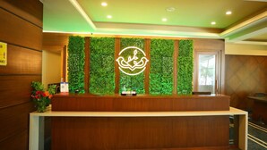 A reception desk with a green wall and a logo, wooden paneling, and a carpeted floor. - Renest Gandhidham (Gandhidham)