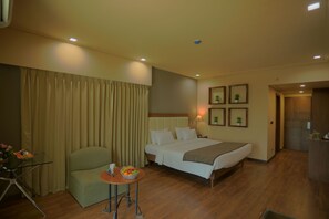 A hotel room with a bed, a desk, a chair, a small table with fruit, and a curtain. - Renest Gandhidham (Gandhidham)