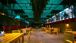 An indoor dining area with wooden tables and chairs, potted plants, and a tiled floor. - Renest Gandhidham (Gandhidham)