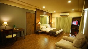 A hotel room with a bed, a desk, a chair, a TV, and an air conditioning unit. - Renest Gandhidham (Gandhidham)