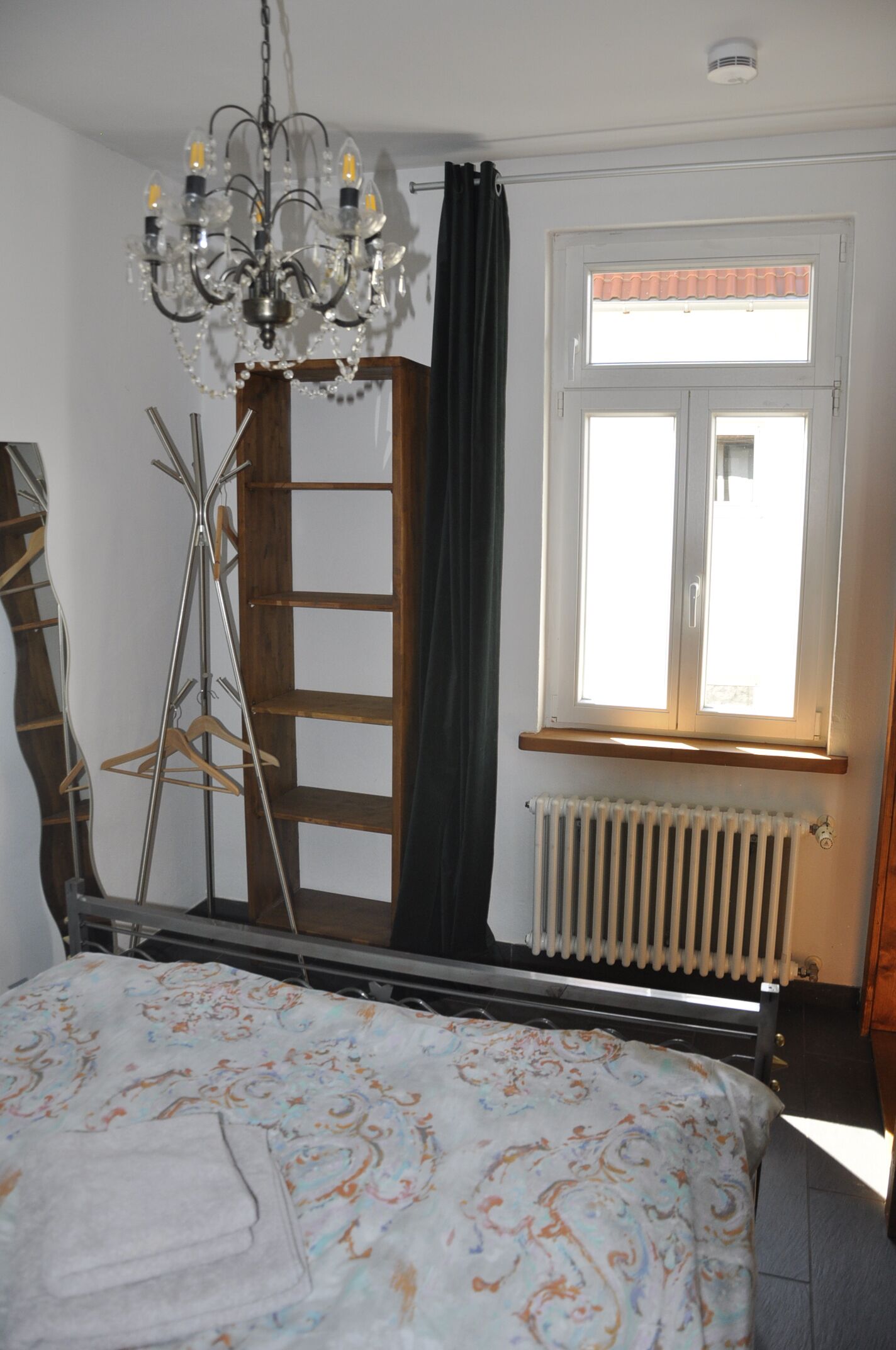 Un dormitorio con cama, un radiador, una ventana con cortinas y una araña.