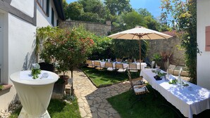 An outdoor patio with round tables set for dining, surrounded by lush greenery and stone walls. - Geibelhof (Karben)