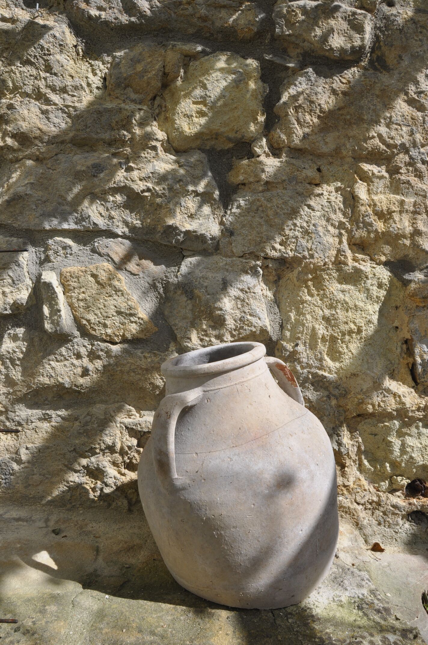Una olla de fang gran i desgastada al costat d'una pared de pedra tova.