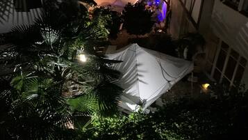 A courtyard with a tent, surrounded by lush greenery and a building with exposed wooden beams.
