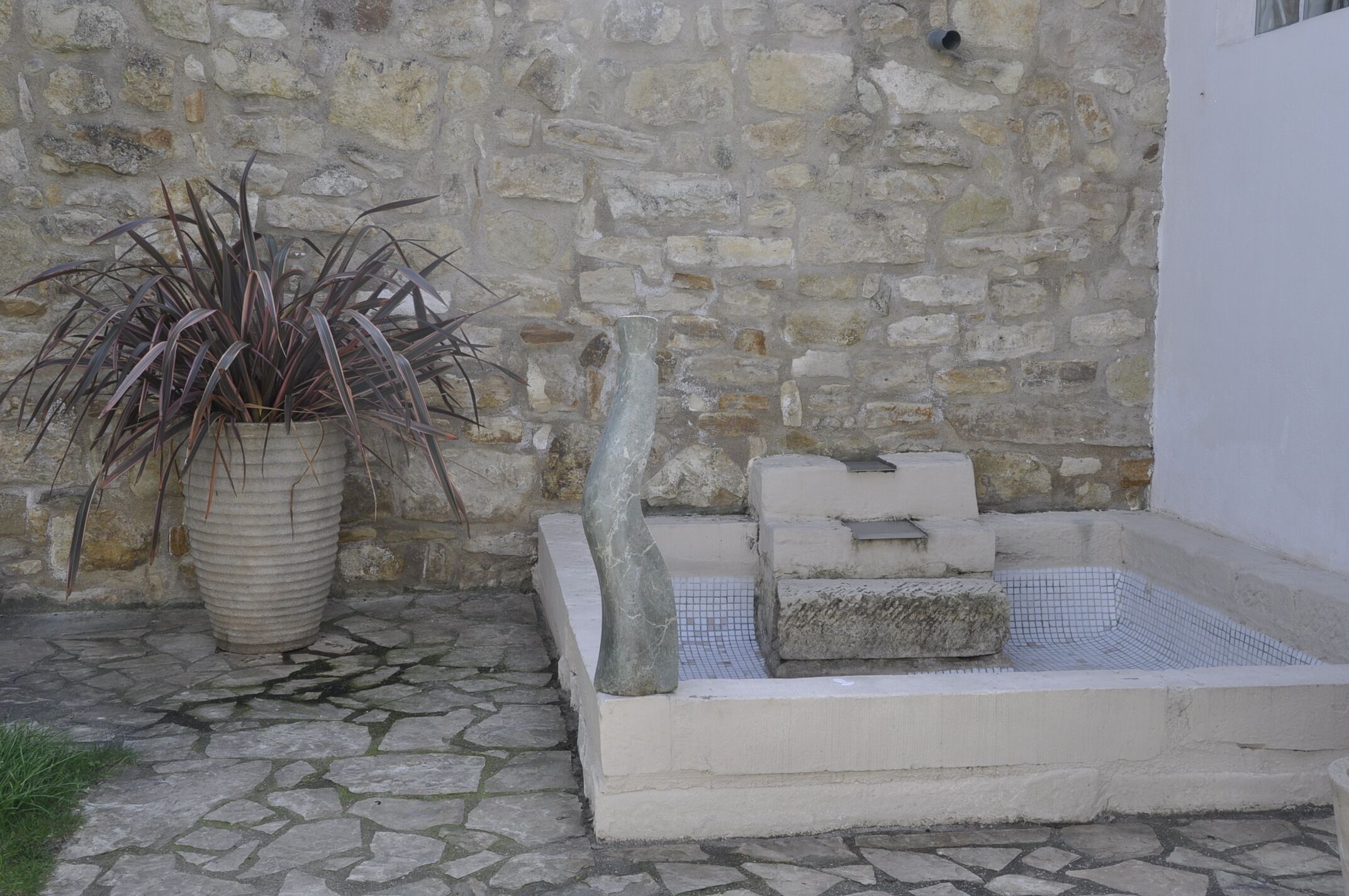 A stone wall, a large potted plant, and a stone basin with a small stone structure.