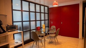 Une cuisine moderne dotée d’une grande fenêtre, d’un mur d’accent rouge et d’un coin repas avec une table et des chaises en verre.