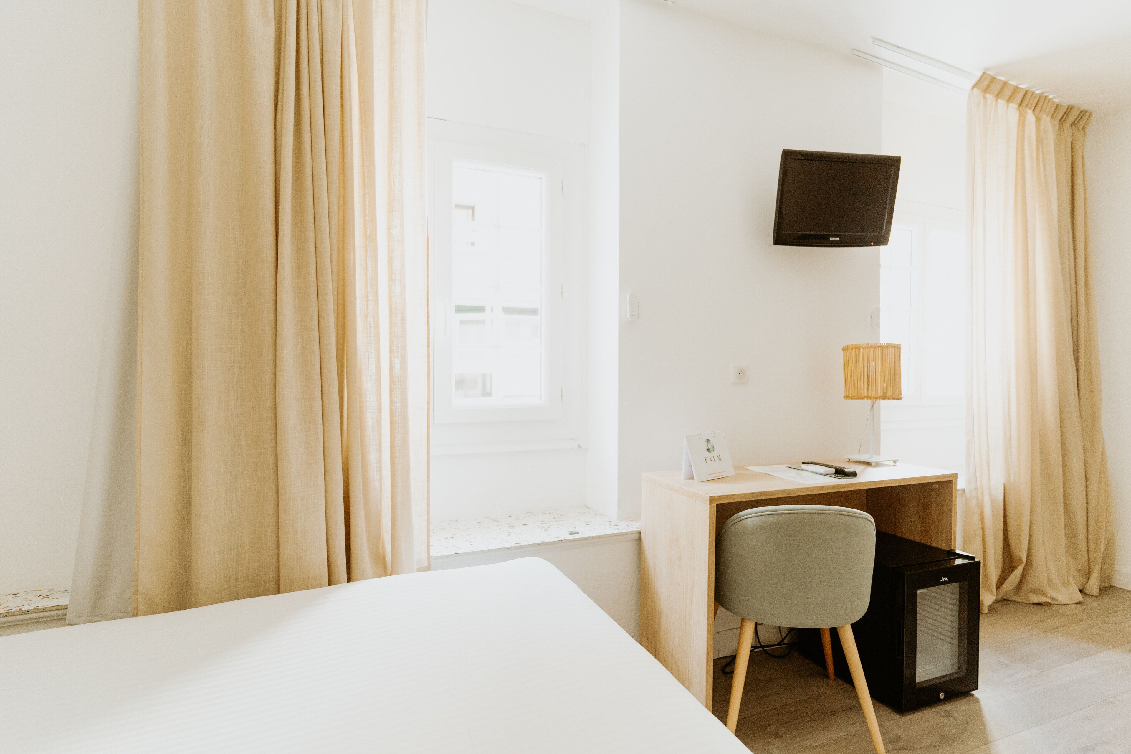 A hotel room with a bed, a desk with a chair, a television, and a lamp.
