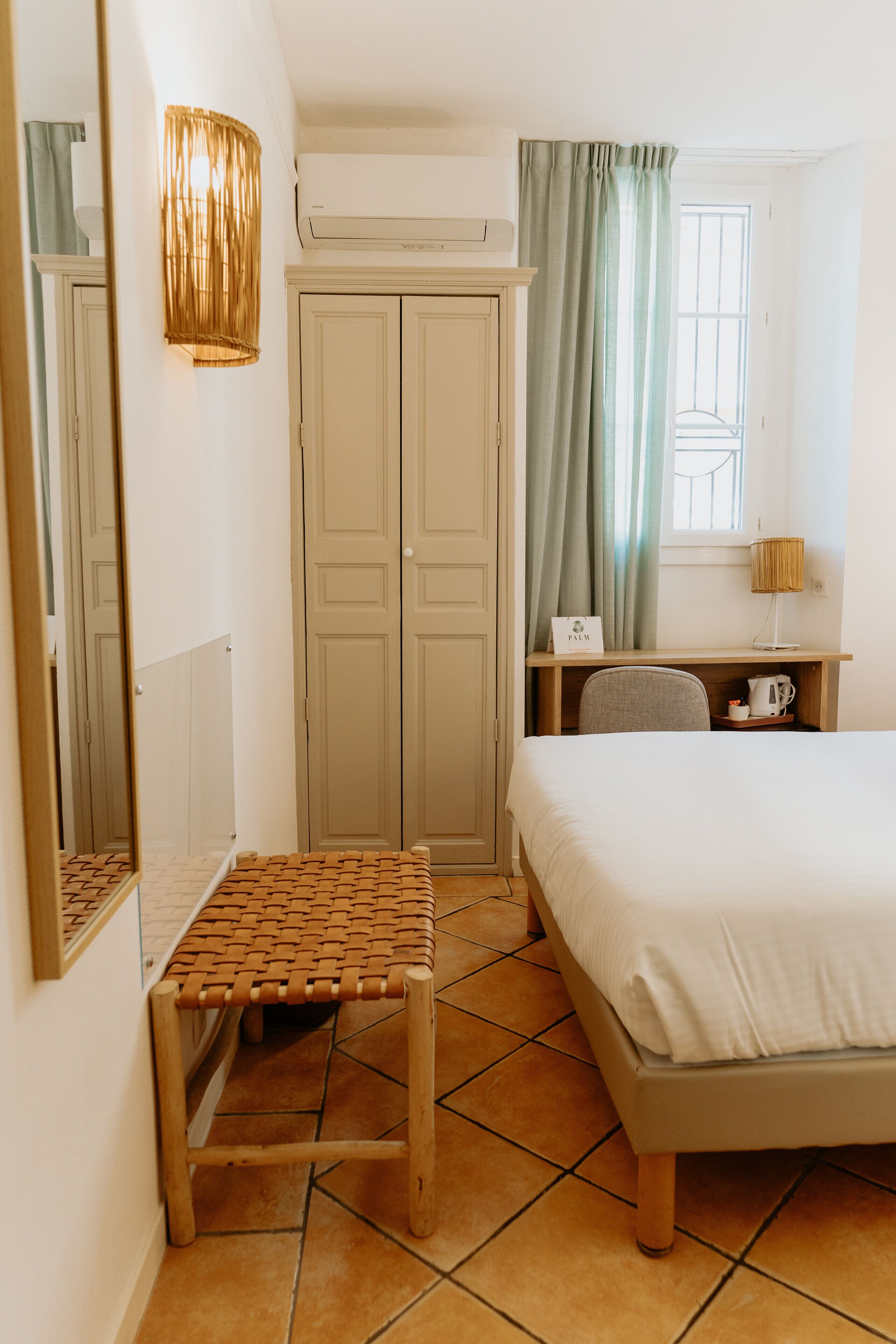 Una habitación de hotel con cama, escritorio, silla, espejo y armario.