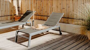 Two sun loungers on a wooden deck with a bamboo fence in the background.