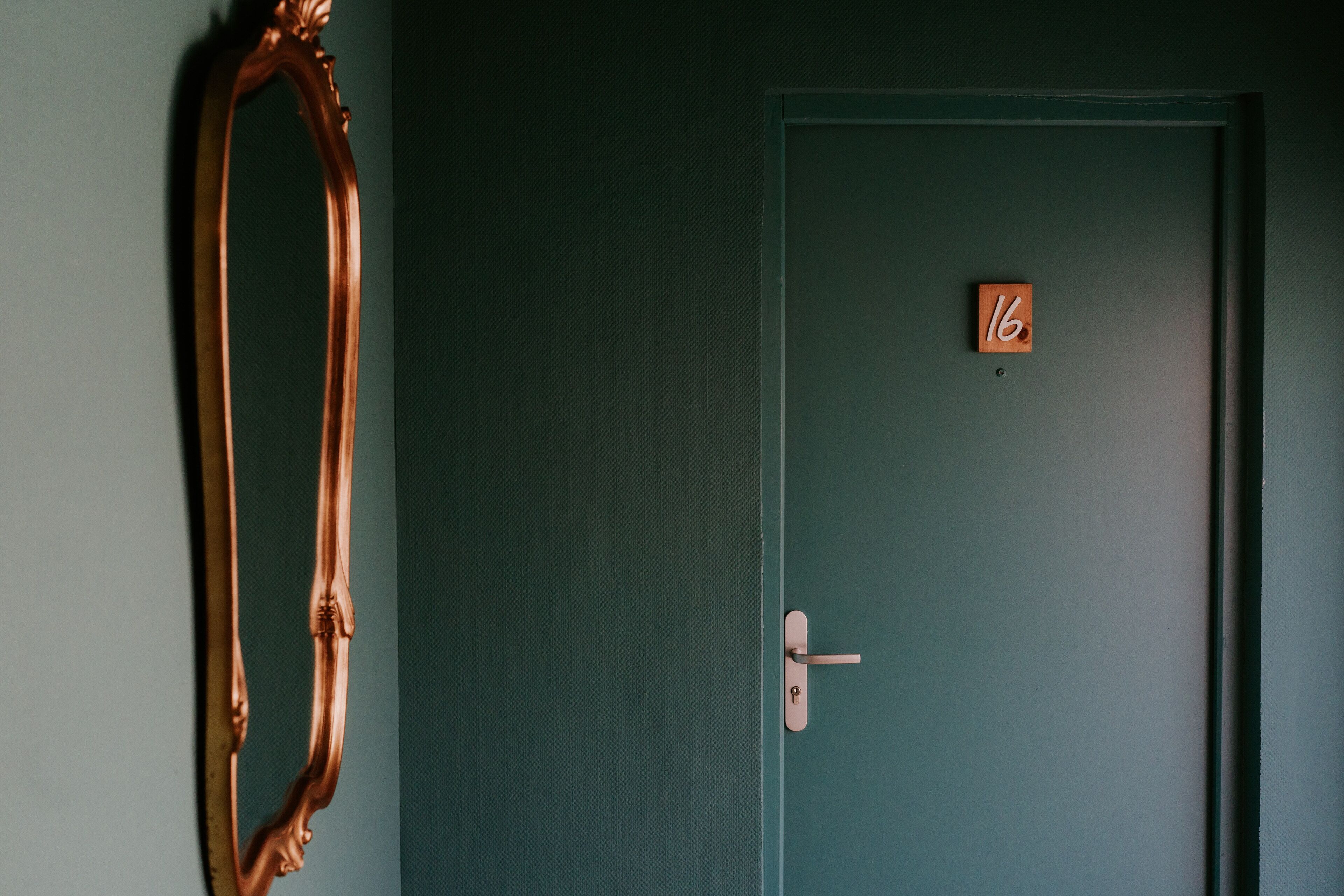 A green door with a number '16' sign, a door handle, and a large mirror on the wall.