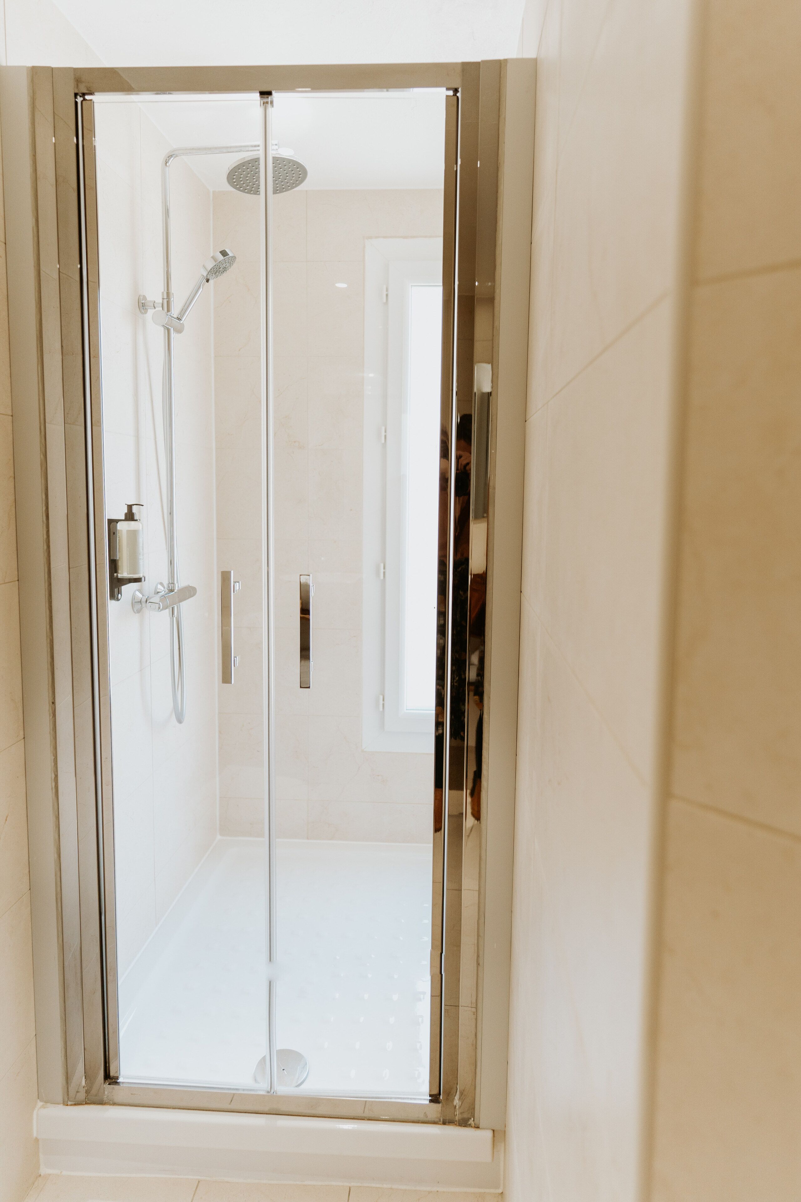 A glass-enclosed shower stall with a handheld showerhead and a wall-mounted faucet.