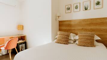 A bedroom with a wooden headboard, two woven pillows, a desk with a chair, and a wall-mounted lamp.