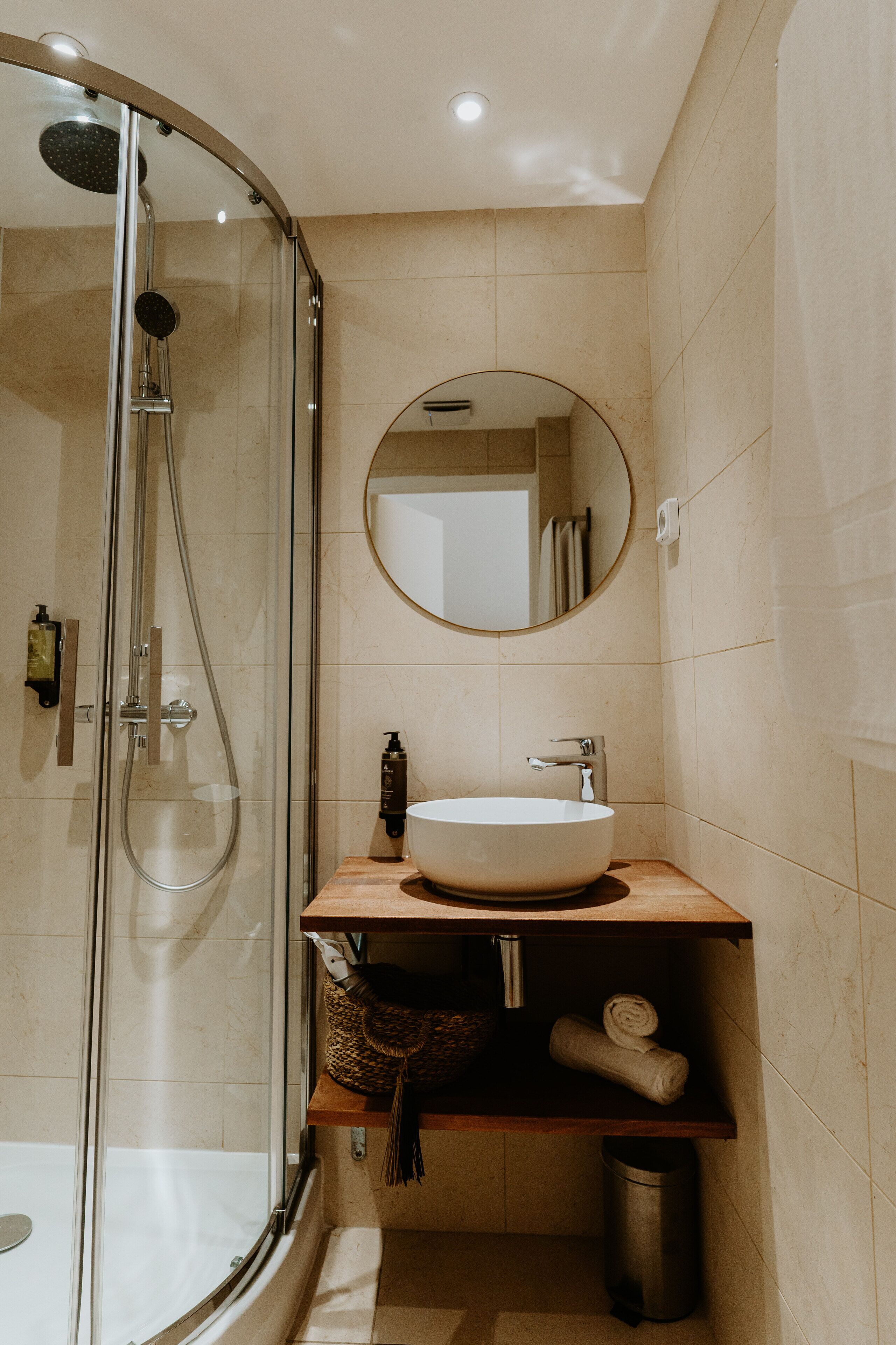 Ein modernes Badezimmer mit einer gläsernen Duschkabine, einem runden Spiegel, einem Holzlagerflächen und einem Waschbecken.
