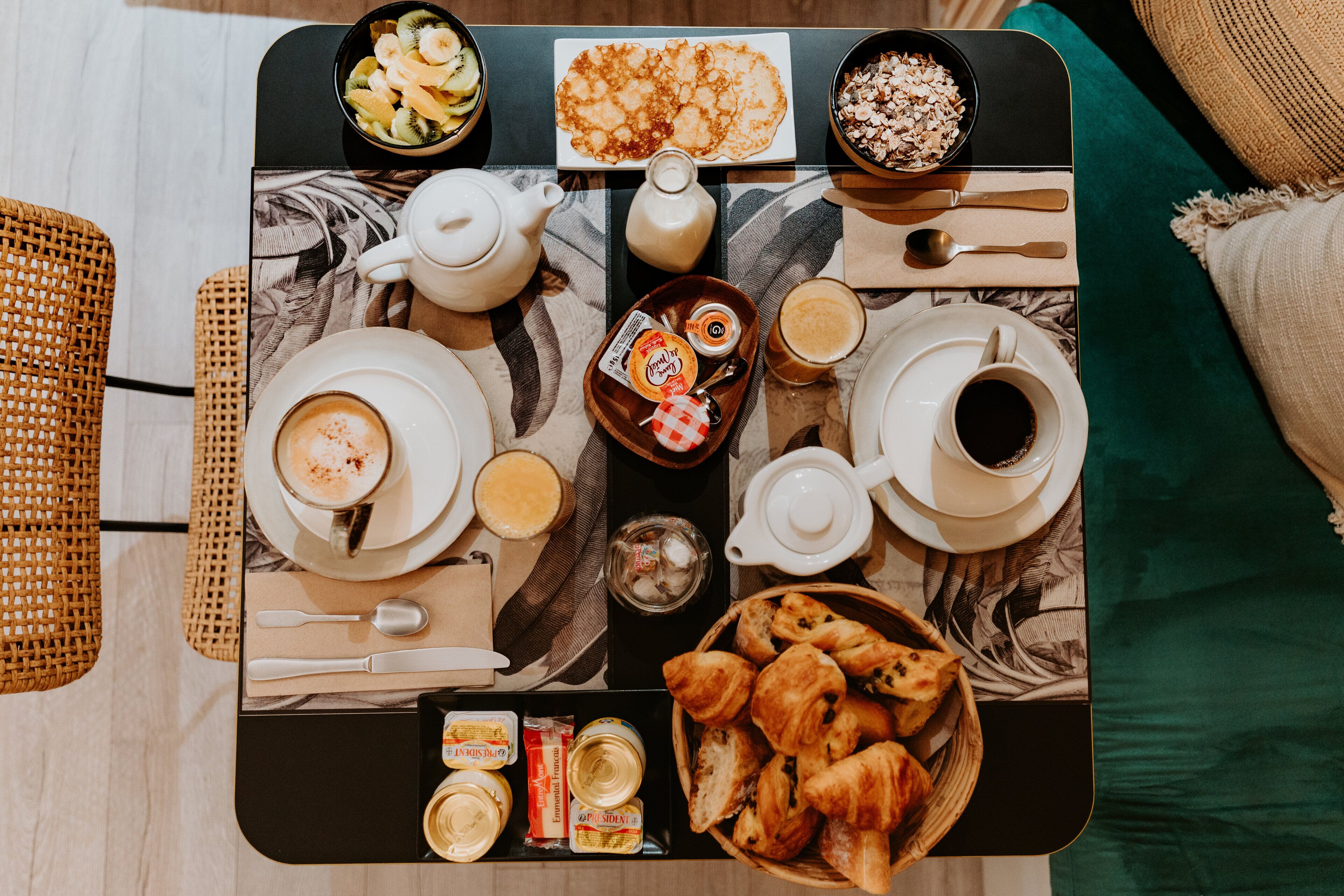 Bandeja de café da manhã com diversos alimentos e bebidas, incluindo croissants, frutas e café, sobre uma mesa com jogo americano.