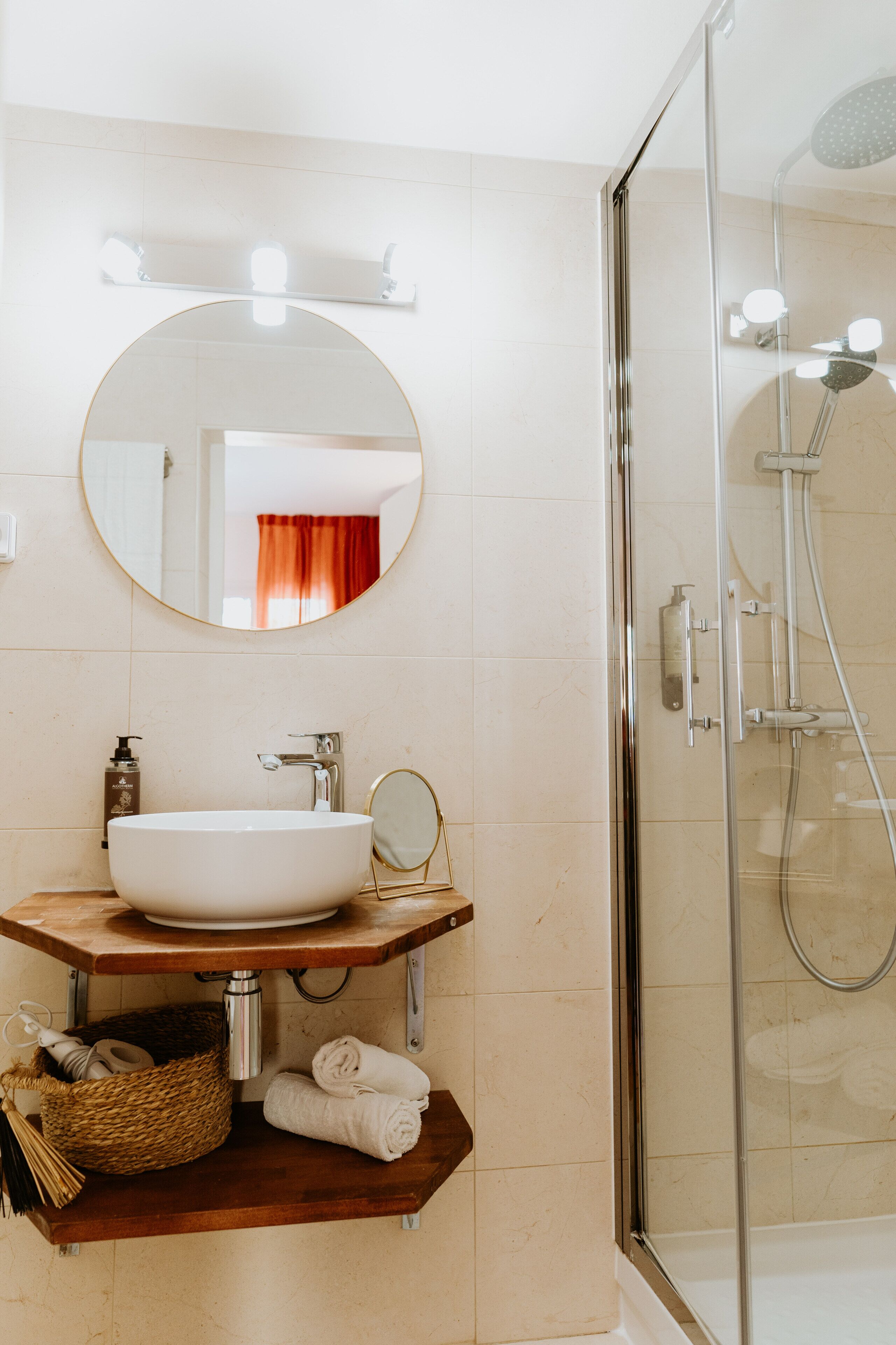 Ein Badezimmer mit rundem Spiegel, weißem Waschbecken und einer Duschkabine.