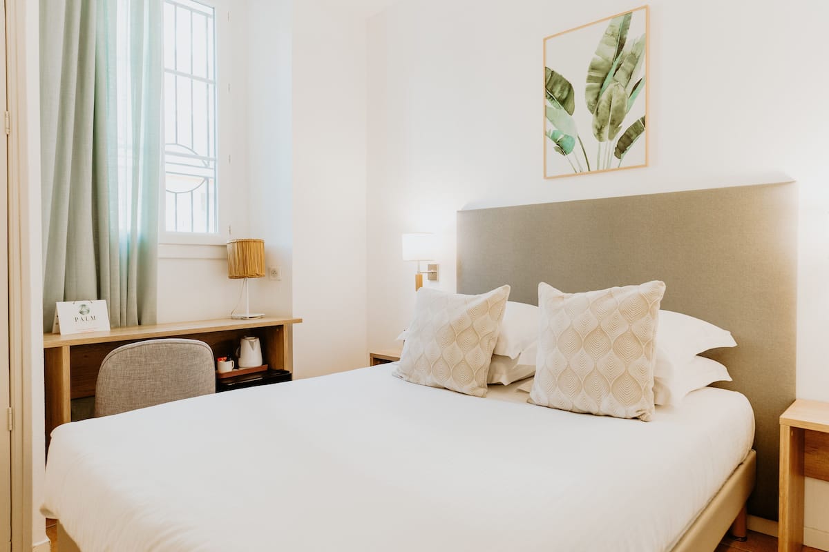 Une chambre d’hôtel avec un grand lit, un bureau, une chaise, une table de chevet, une lampe et une plante décorative accrochée au mur.