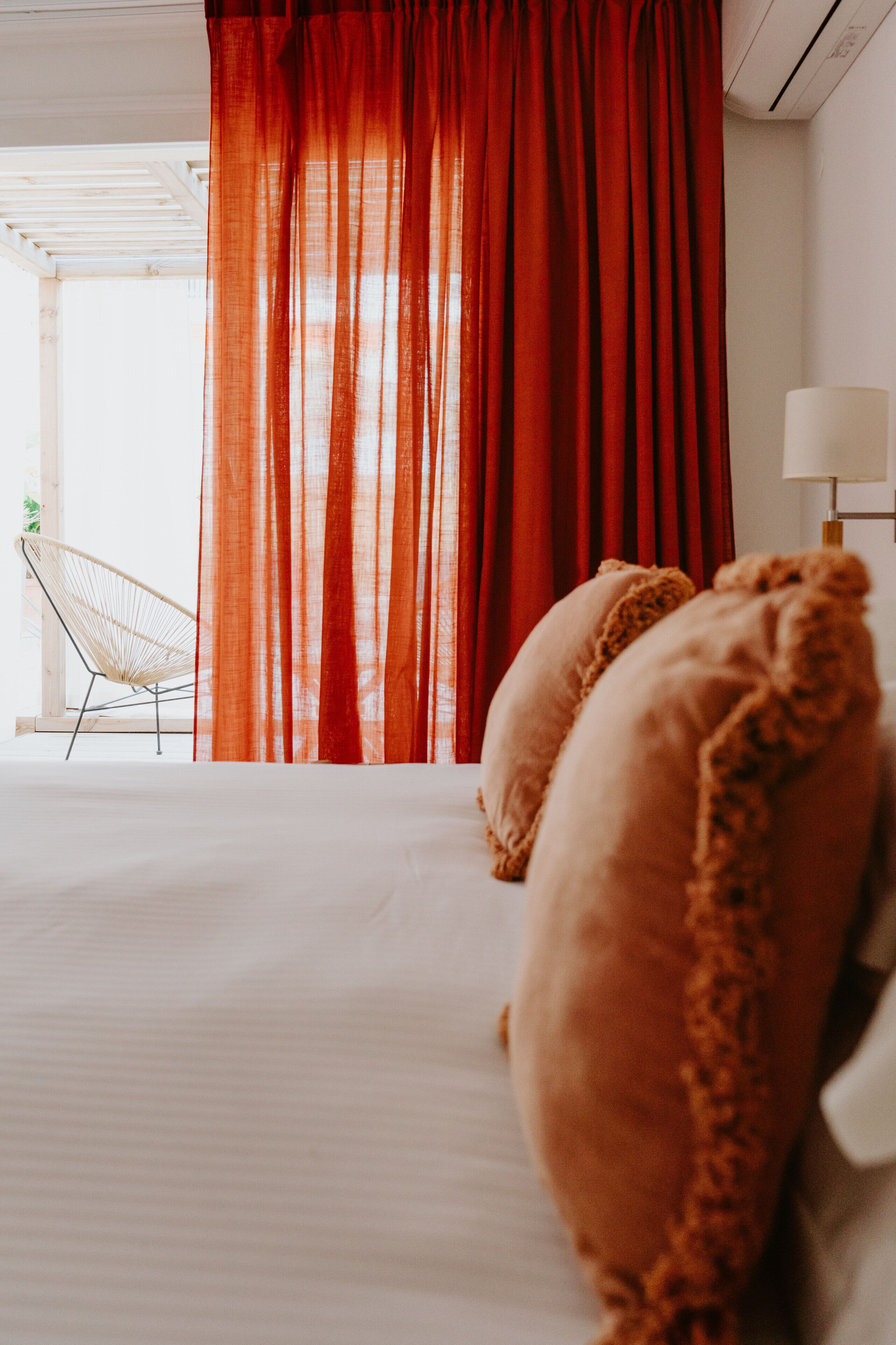 A bedroom with a bed, red curtains, a chair, and a lamp.