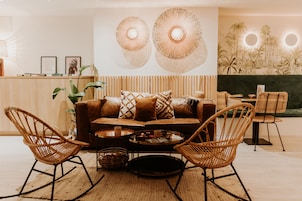 Una sala acogedora con un sofá, dos sillones de mimbre, una mesa de centro y una pared con lámparas circulares.