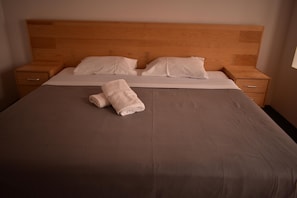 A neatly made bed with a brown bedspread and two white pillows, a wooden headboard, and two bedside tables with drawers.