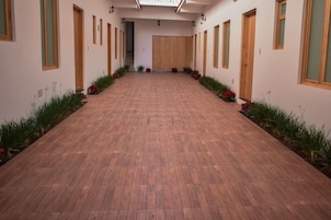 Un pasillo con puertas de madera y suelo de baldosas, bordeado por plantas y flores.