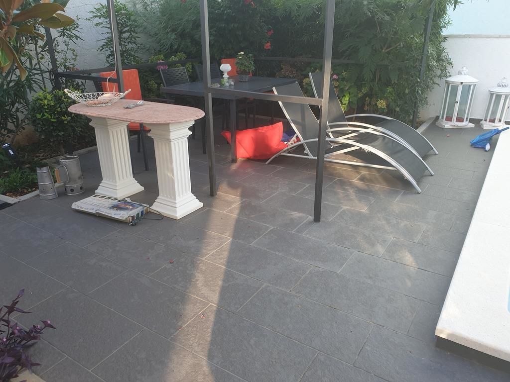 Een buitenterras met een ronde tafel, stoelen en een kleine witte tafel.