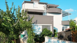 A modern two-story house with a flat roof, solar panels, and a covered outdoor area.