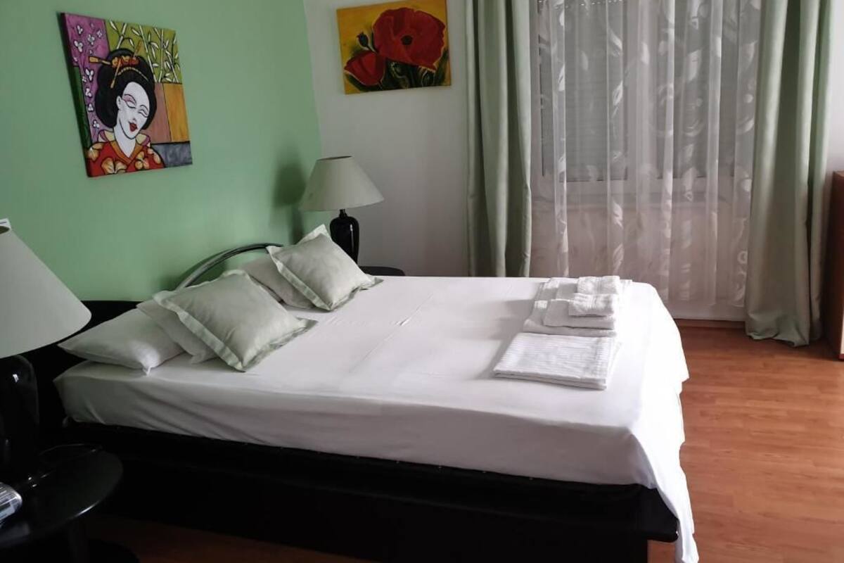 Una cama bien hecha con almohadas y una toalla doblada, una lámpara de noche y obras de arte en las paredes.