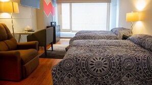 Ett hotellrum med två sängar, ett skrivbord, en stol, en TV och ett stort fönster.