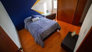 Een slaapkamer met een bed, een nachtkastje, een houten garderobe en een tafeltje met een lamp.
