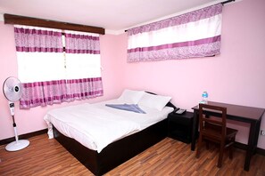 A bedroom with a bed, a desk, a chair, a fan, and a window with curtains.