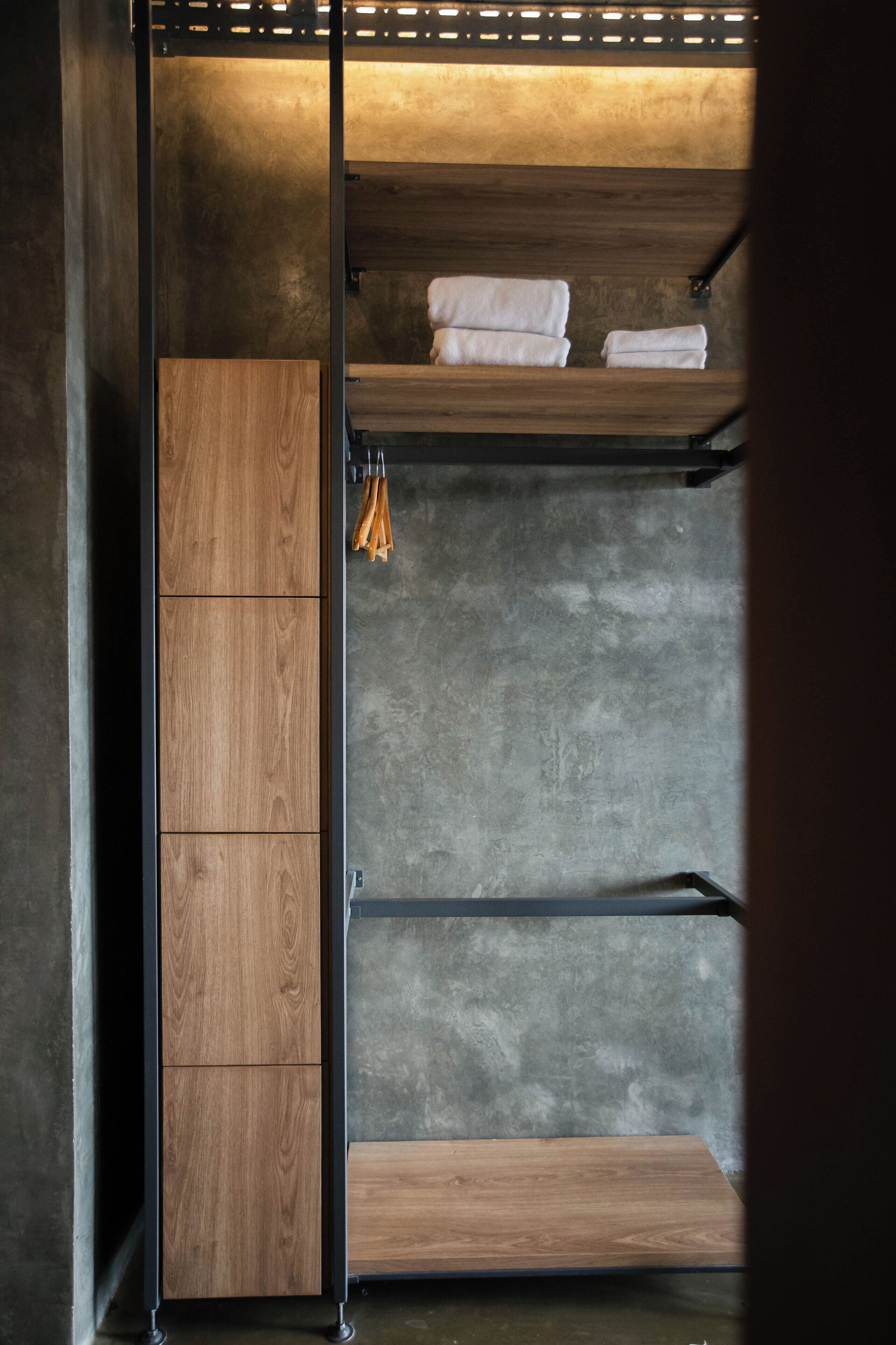 A bunk bed with wooden panels and metal railings, a wooden wardrobe, and a concrete wall.