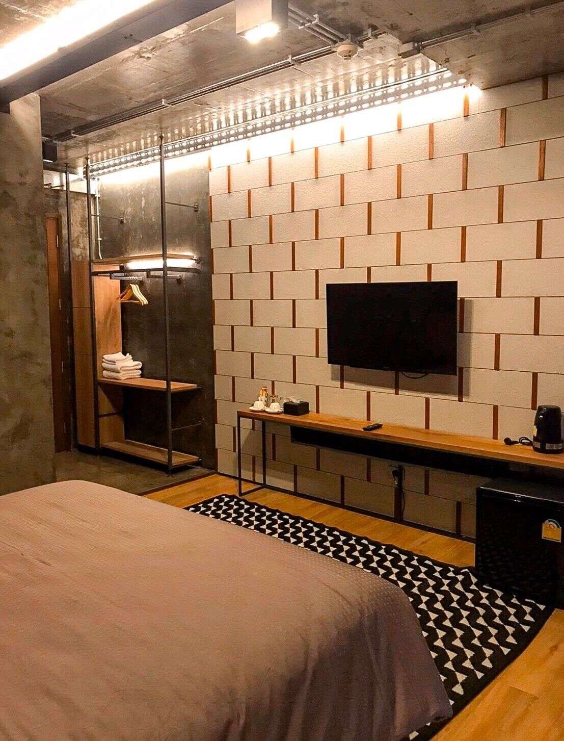 Una habitación de hotel moderna con cama, televisor montado en la pared, escritorio de madera y espejo.