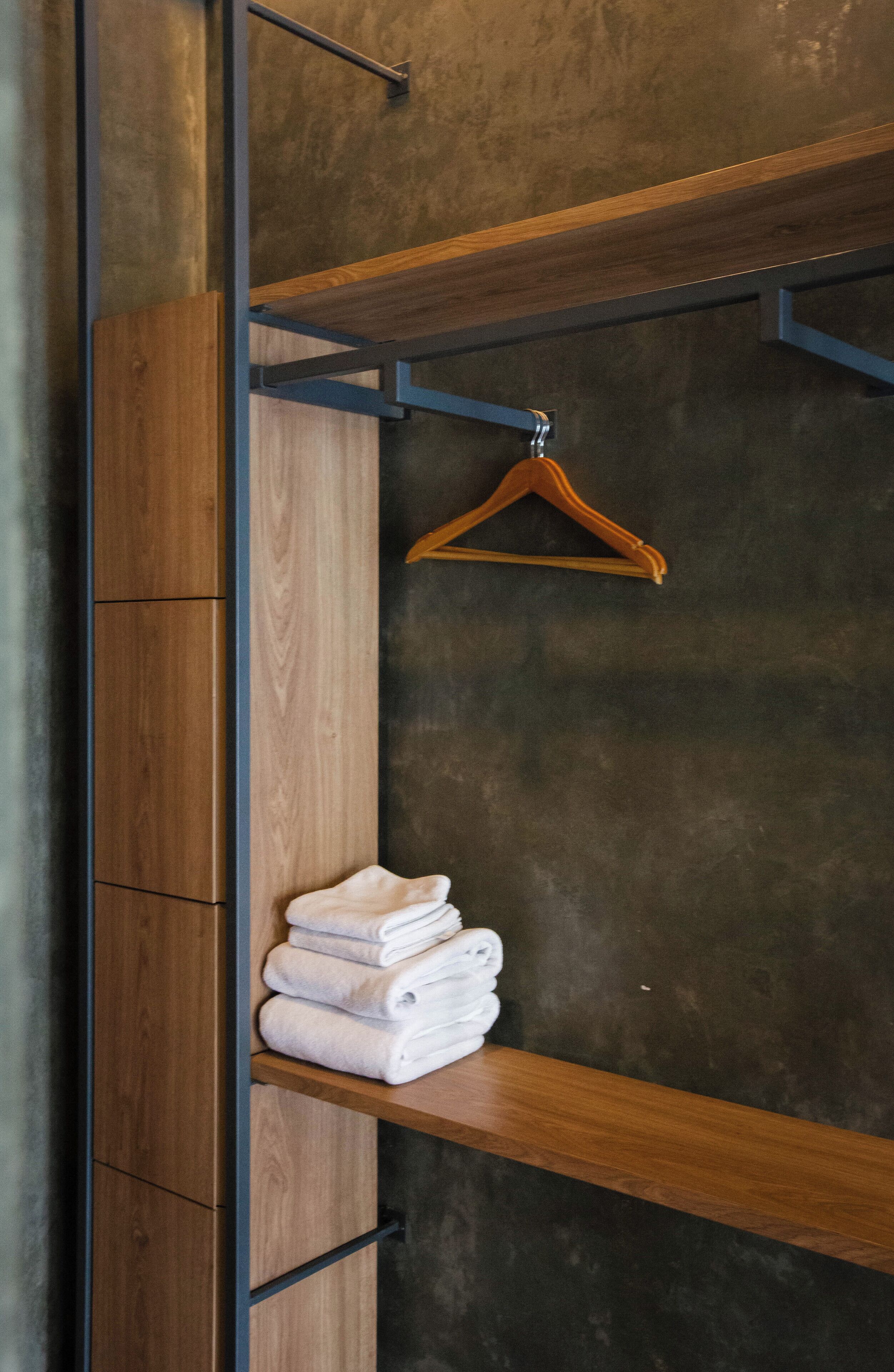 A wooden wardrobe with a hanging rod and a shelf with folded towels.