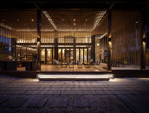 An outdoor seating area with tables and chairs, a wooden pergola structure, and a stone pathway.