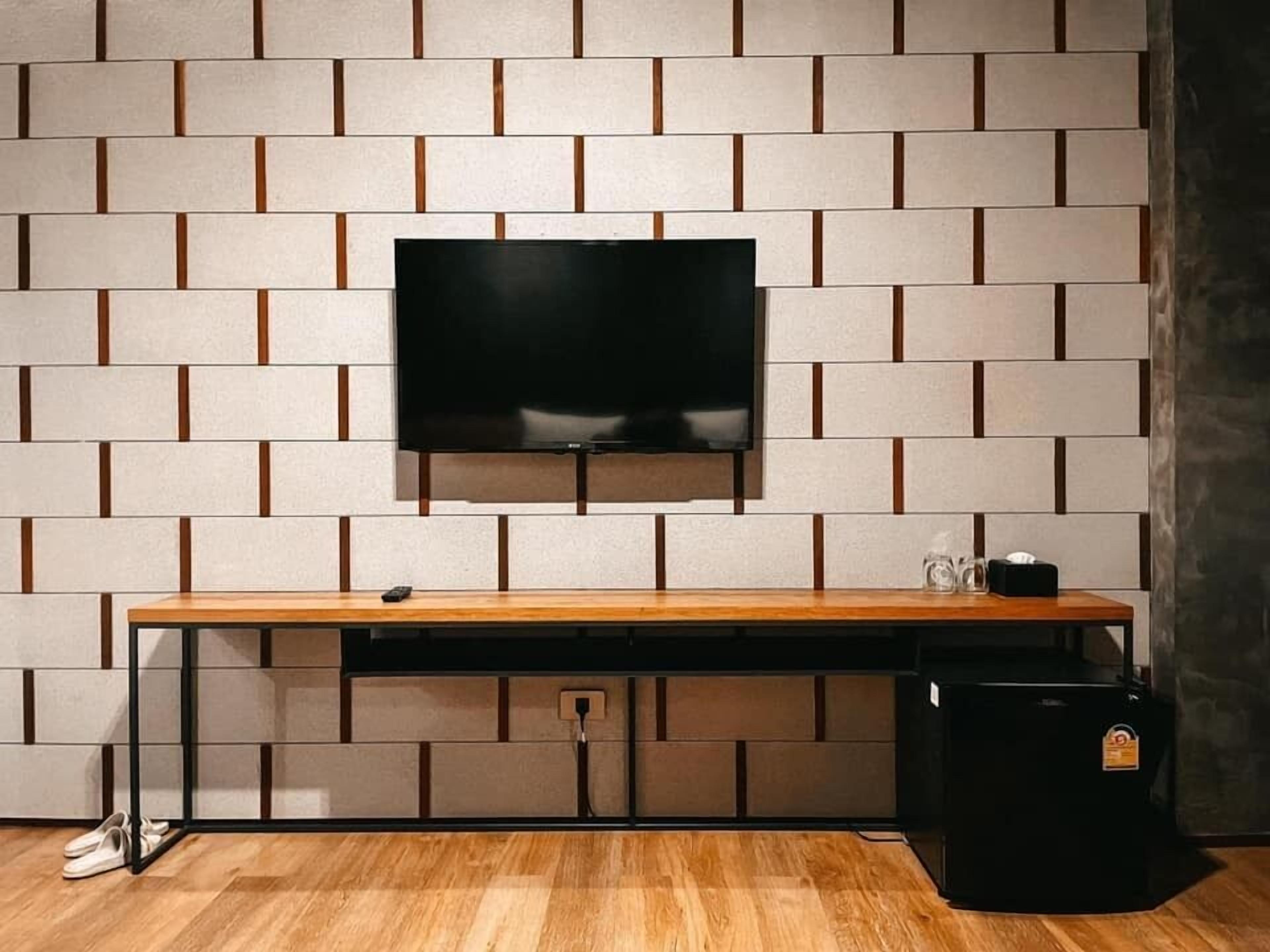 A modern room with a flat-screen TV mounted on a brick-patterned wall, a wooden desk with a remote control, and a black storage unit.