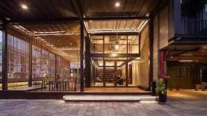 A modern building entrance with a glass door, wooden steps, and a seating area with chairs and tables. - Navakitel Design Hotel (Nakhon Si Thammarat)