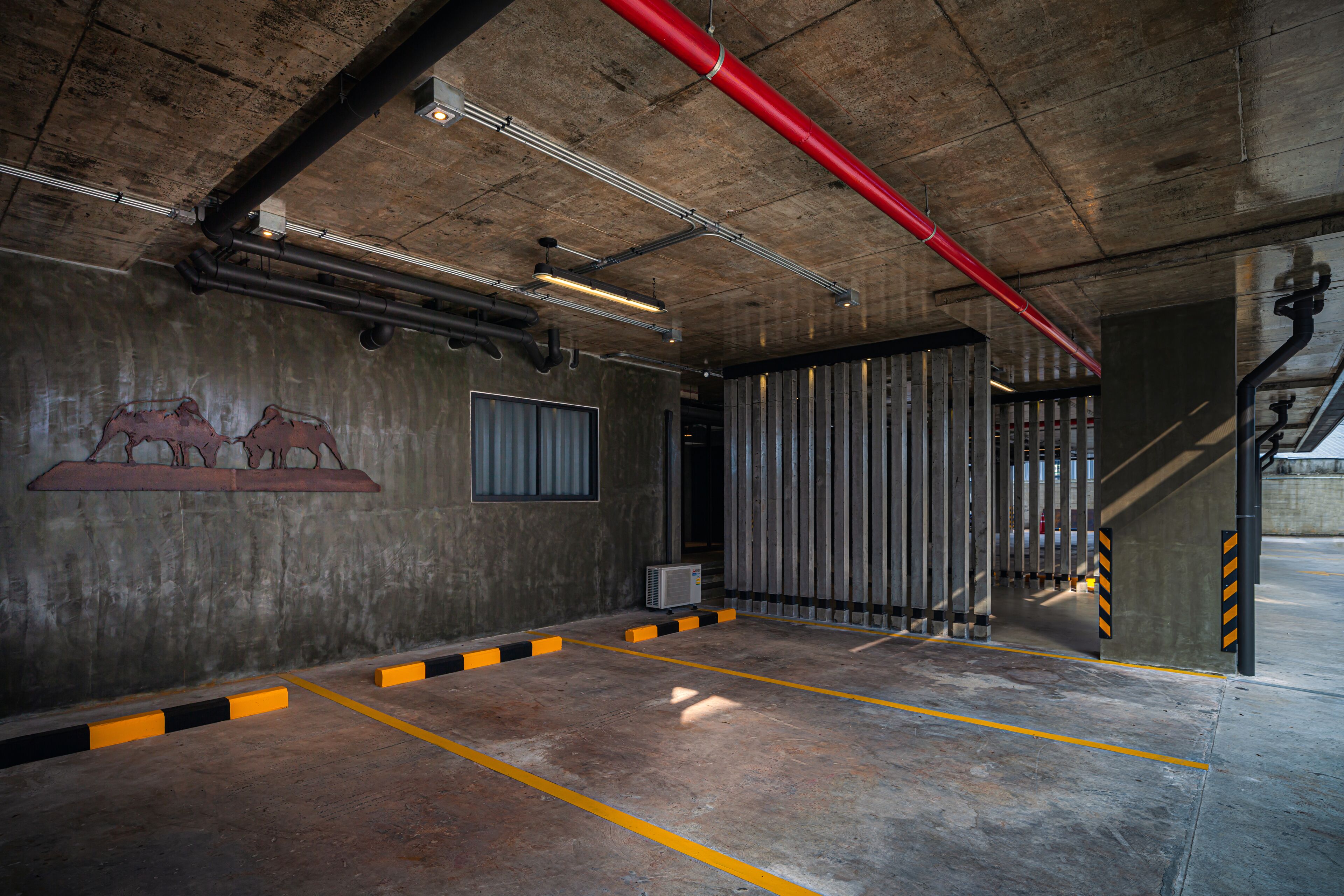 Un parking de style industriel, avec des murs en béton, des garde-corps en métal et un tuyau rouge au plafond.