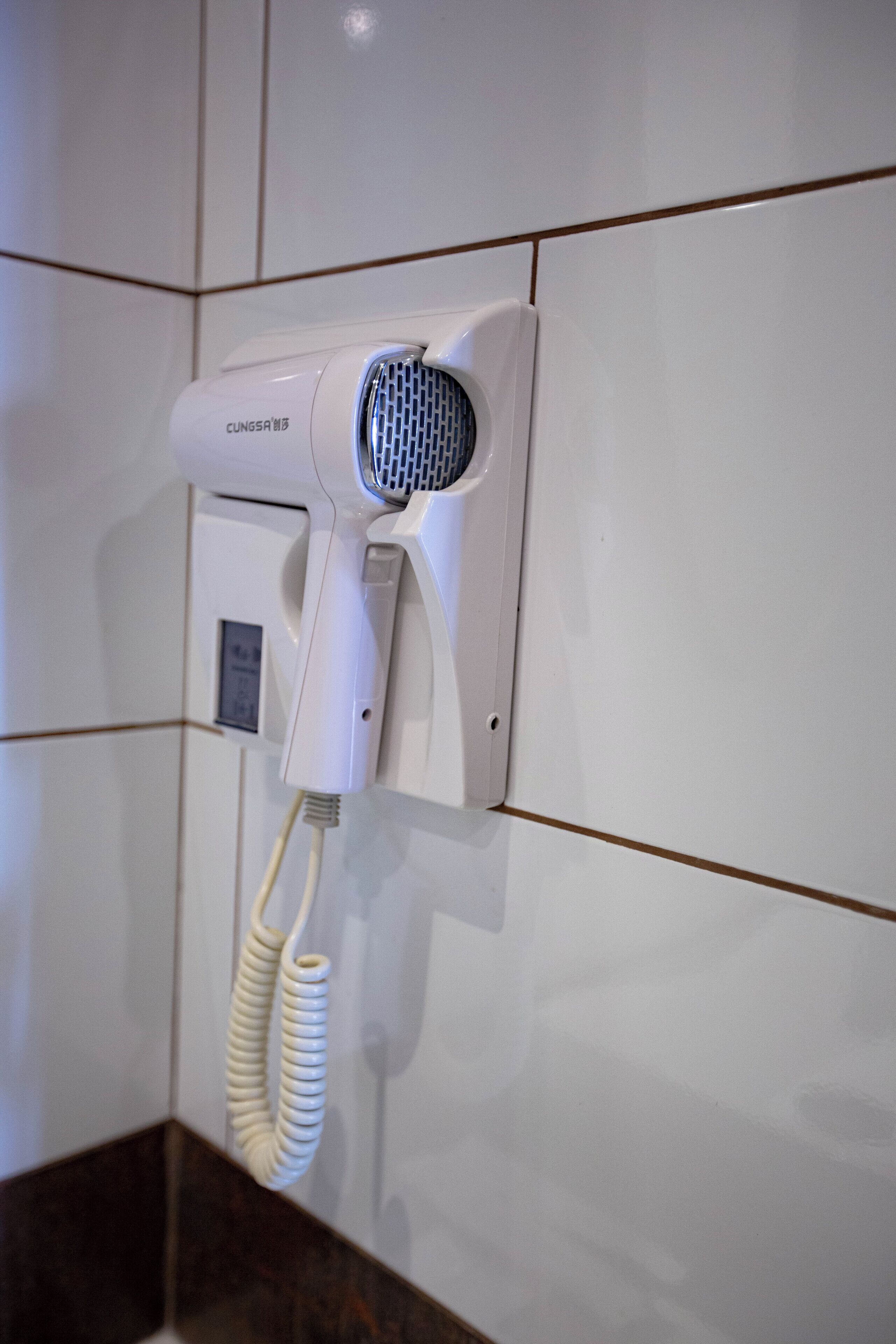 A wall-mounted hairdryer with a control panel and a coiled cord.