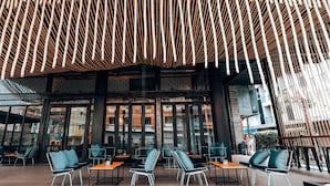 An outdoor seating area with modern chairs and tables, a wooden slatted ceiling, and large windows offering views of the city. - Navakitel Design Hotel (Nakhon Si Thammarat)