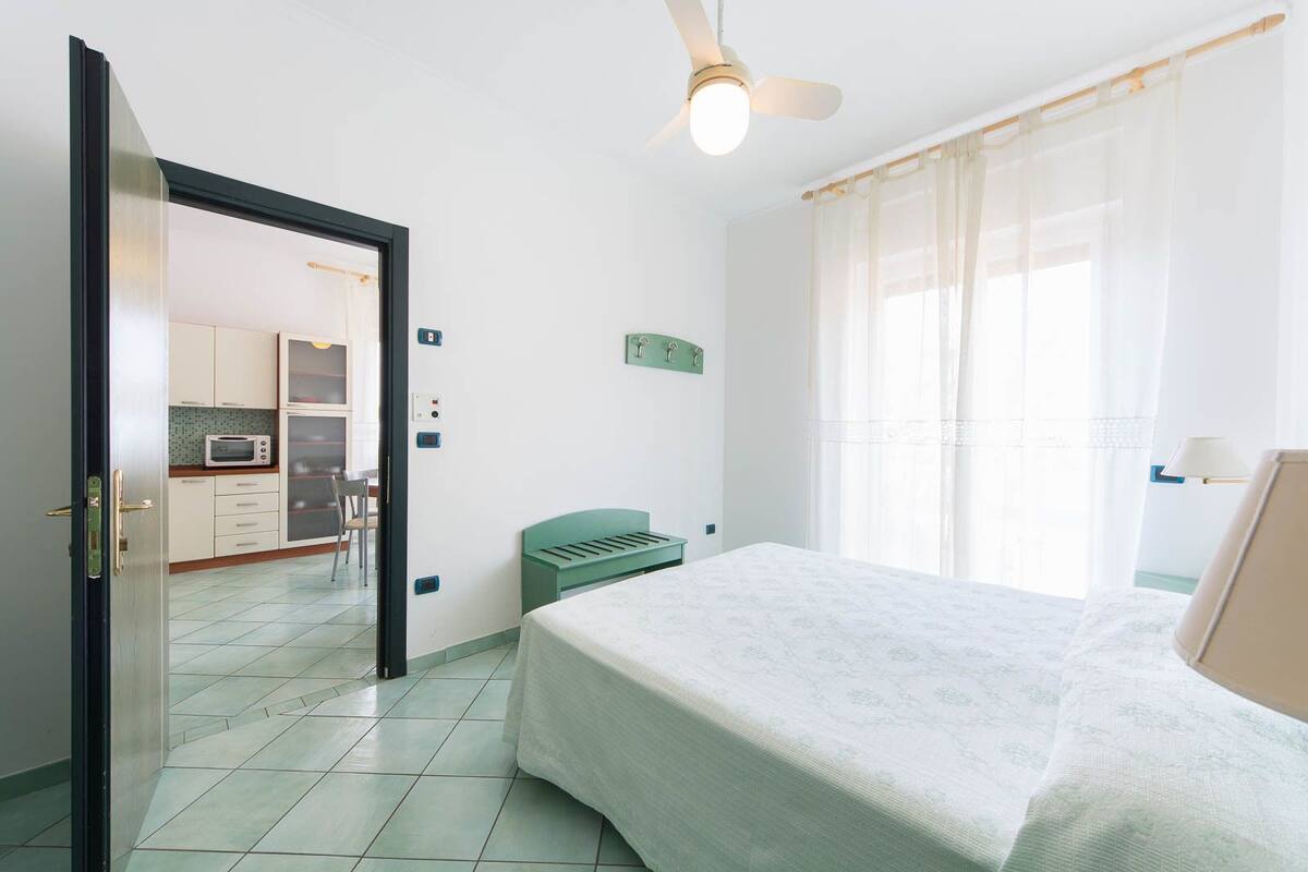 A hotel room with a bed, a desk, a chair, a kitchenette, and a bathroom.