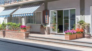 A hotel entrance with a covered outdoor seating area, a brick wall, and flower planters. - La Residenza Aparthotel (Maiori)